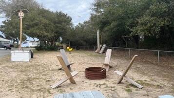 An outdoor seating area with wooden chairs and a picnic table, surrounded by trees and a fence.