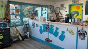 Een receptiegedeelte met een balie waarop diverse spullen staan, een raam met decoraties, en een muur met geschilderde schedels.