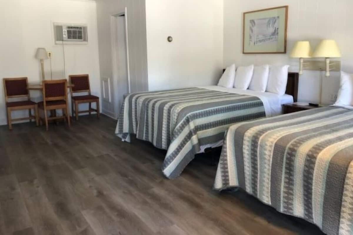 A hotel room with two beds, a desk, chairs, and a lamp.
