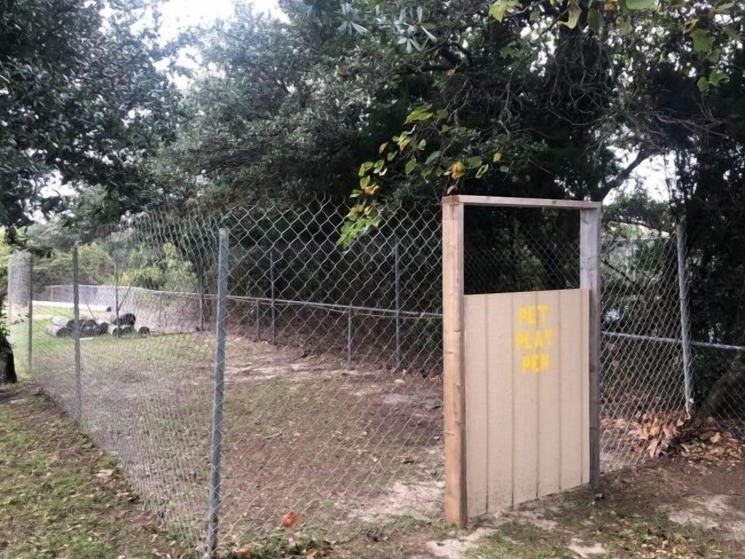 A chain-link fence with a wooden gate, a grassy area, and trees in the background.