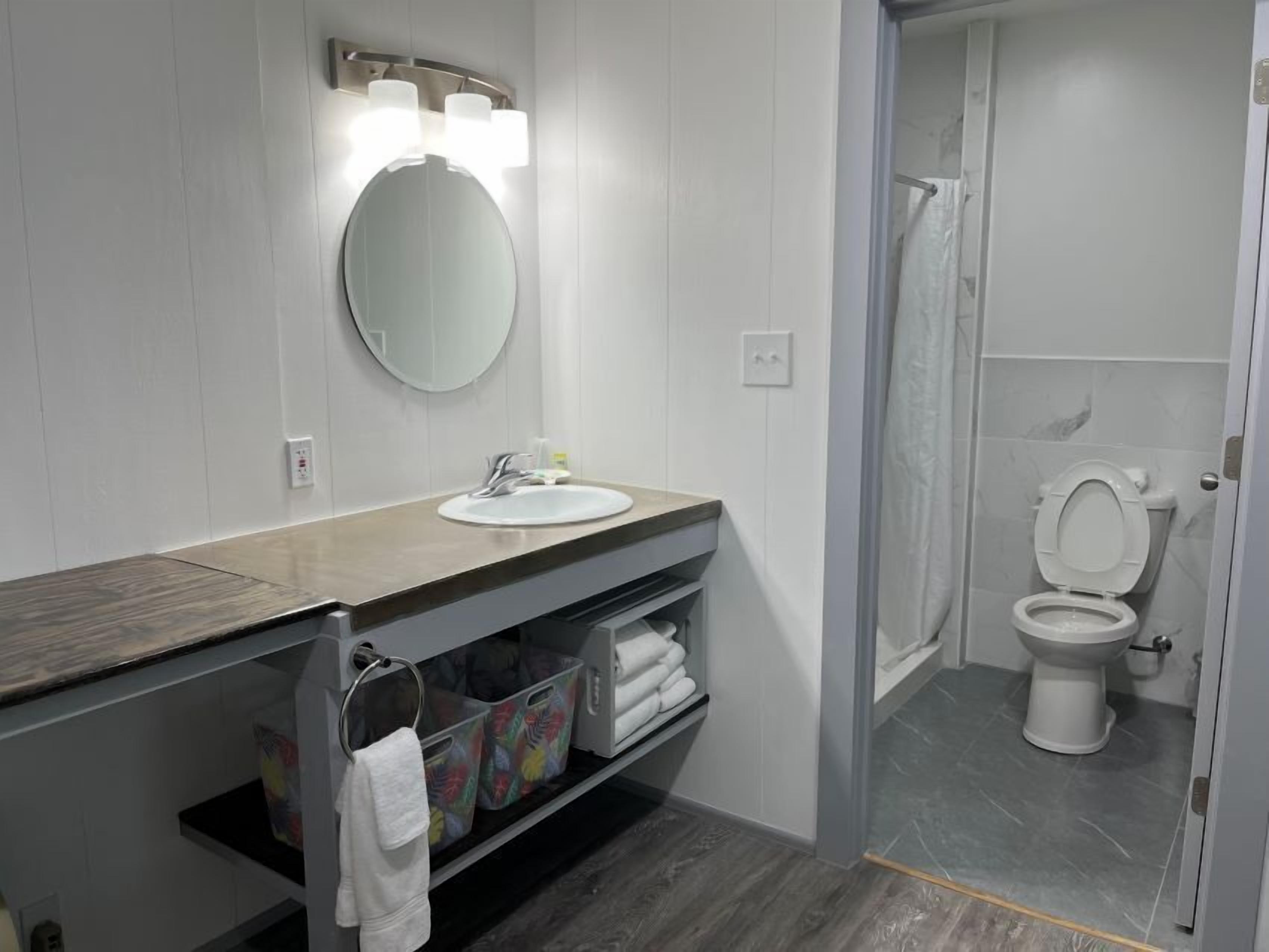 A modern bathroom with a wooden vanity, a round mirror, and a toilet.
