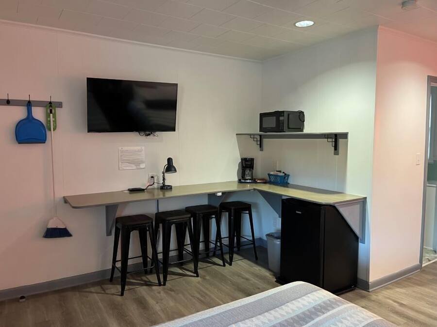 A compact kitchenette with a microwave, coffee maker, and a TV mounted on the wall. There are three stools and a small refrigerator.