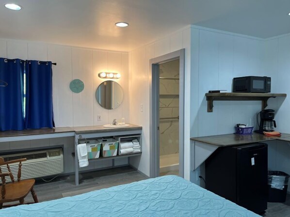 A compact hotel room with a bed, a small desk with a microwave, a sink, and a mirror. - Swell Motel (Buxton)