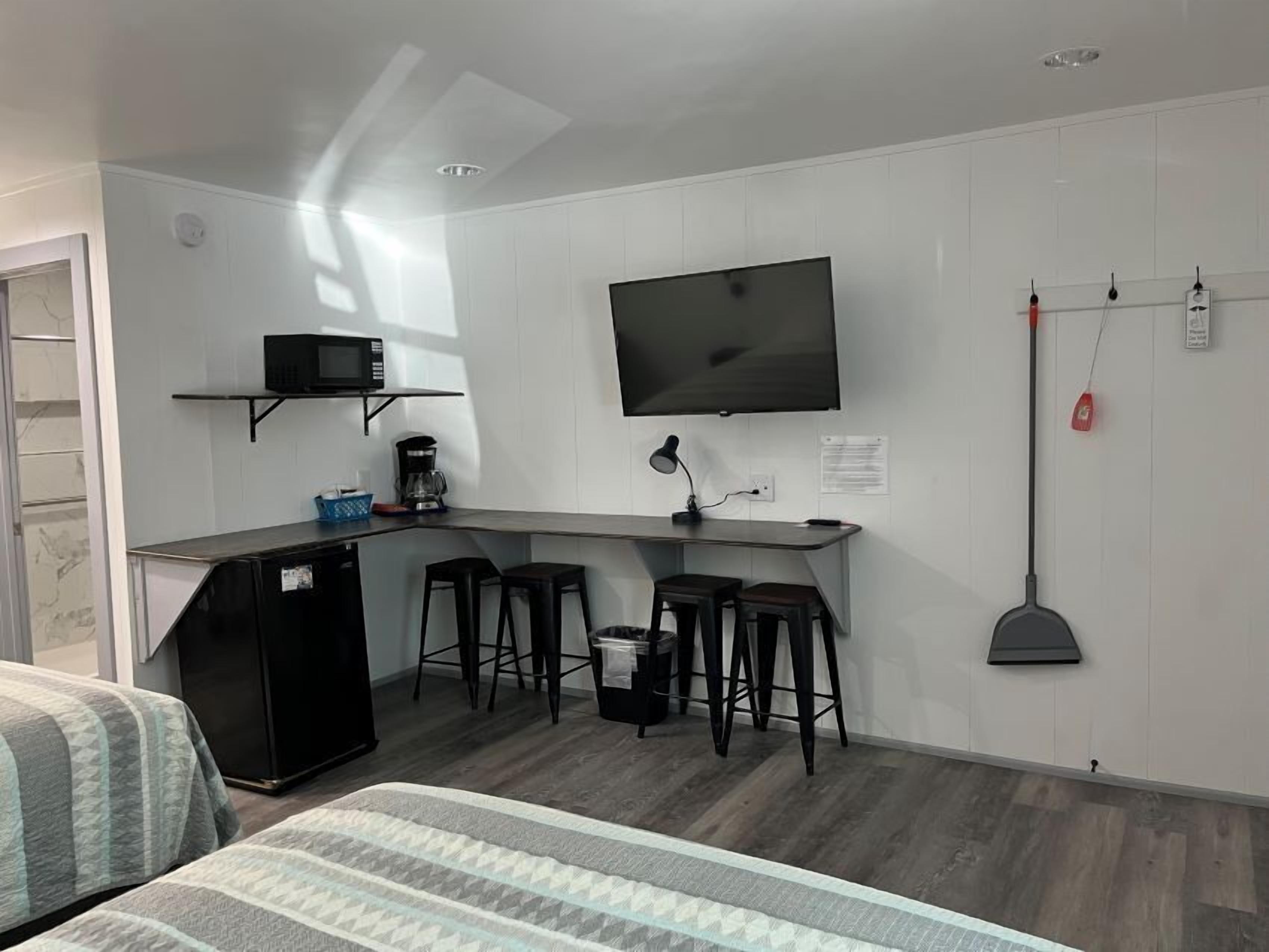 A compact room with a kitchenette, a TV mounted on the wall, and a bed with striped bedding.