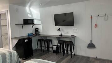 A compact room with a kitchenette, a TV mounted on the wall, and a bed with striped bedding.