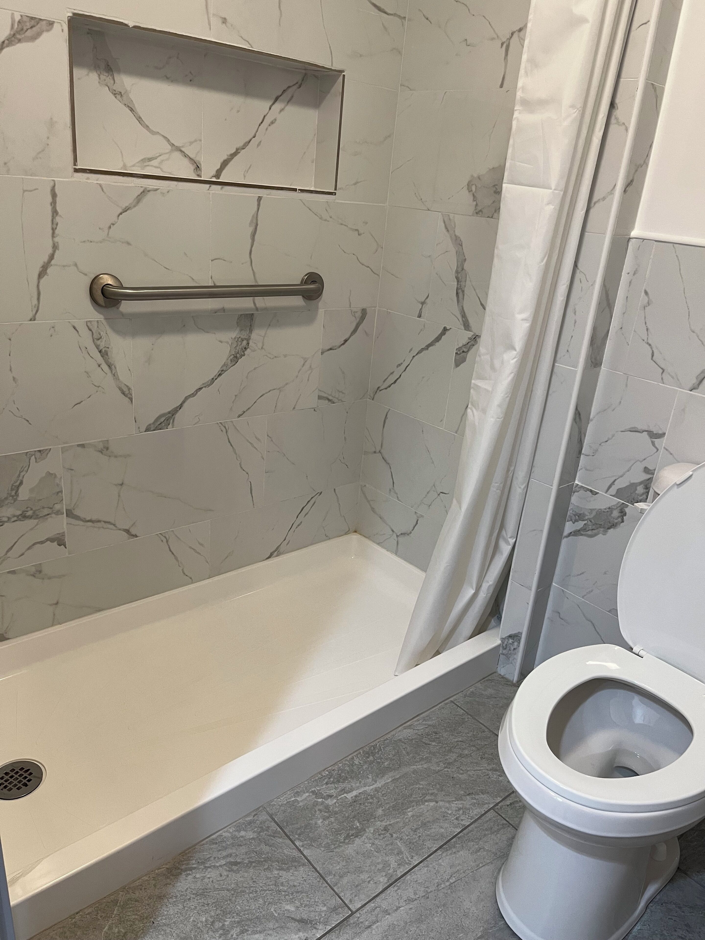 A bathroom with a shower, toilet, and marble-tiled walls.