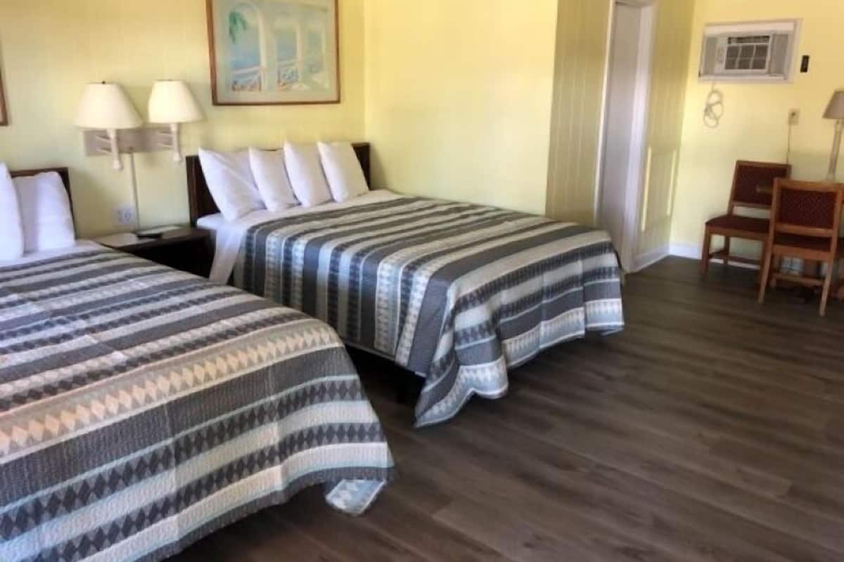 A hotel room with two beds, a desk, a chair, a painting on the wall, and a door.