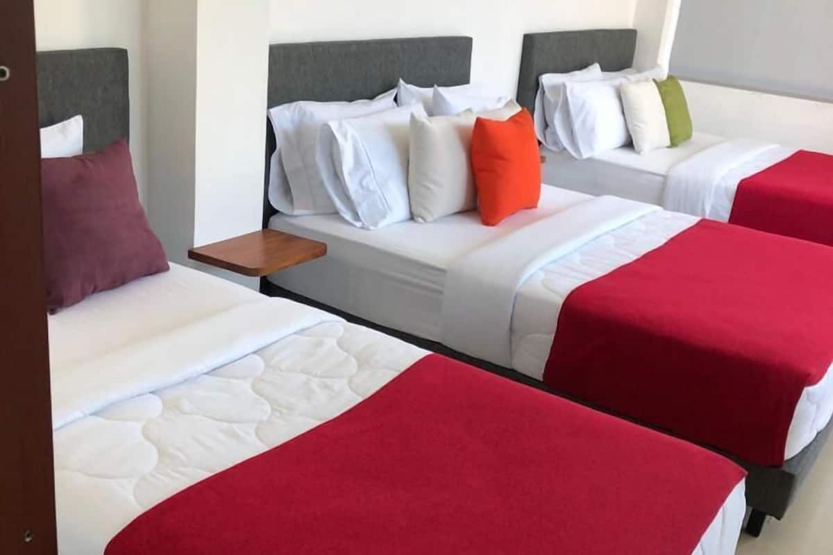 A hotel room with three beds, each with a red bedspread and white bedding. There are two framed pictures on the wall above the beds.