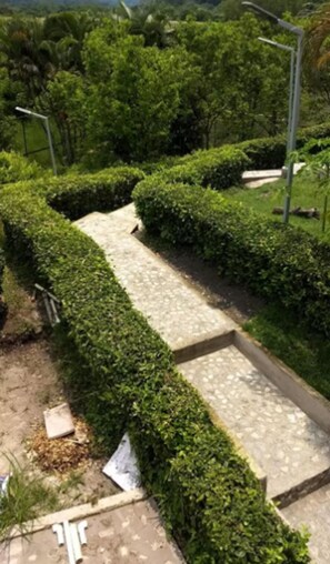 A landscaped garden with a paved walkway, neatly trimmed hedges, and a street lamp. - Hotel Spa Excalibur (Villeta)