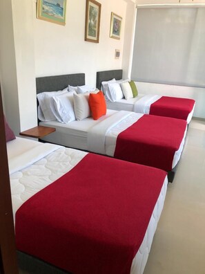 A hotel room with three beds, each with a red bedspread and white bedding. There are two framed pictures on the wall above the beds. - Hotel Spa Excalibur (Villeta)
