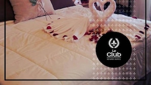 Ein Hotelzimmer mit einem ordentlich bezogenen Bett, einem gepolsterten Kopfteil und einer dekorativen Anordnung aus Handtüchern und Blumen in Herzform.