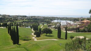 En golfbane med et vandareal, ciprusskove og havudsigt.