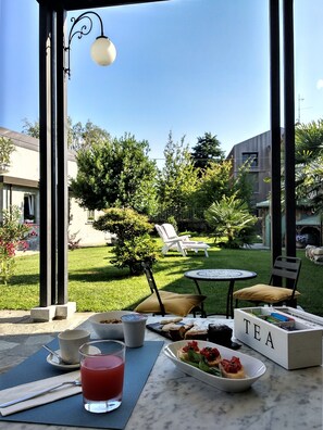 Un espace de restauration en plein air avec une table dressée pour deux personnes, un verre d’une boisson rouge et une boîte à thé étiquetée « THÉ ».
