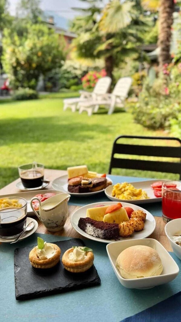 Une table dressée à l’extérieur, avec divers plats et boissons, entourée de verdure et d’un jardin.