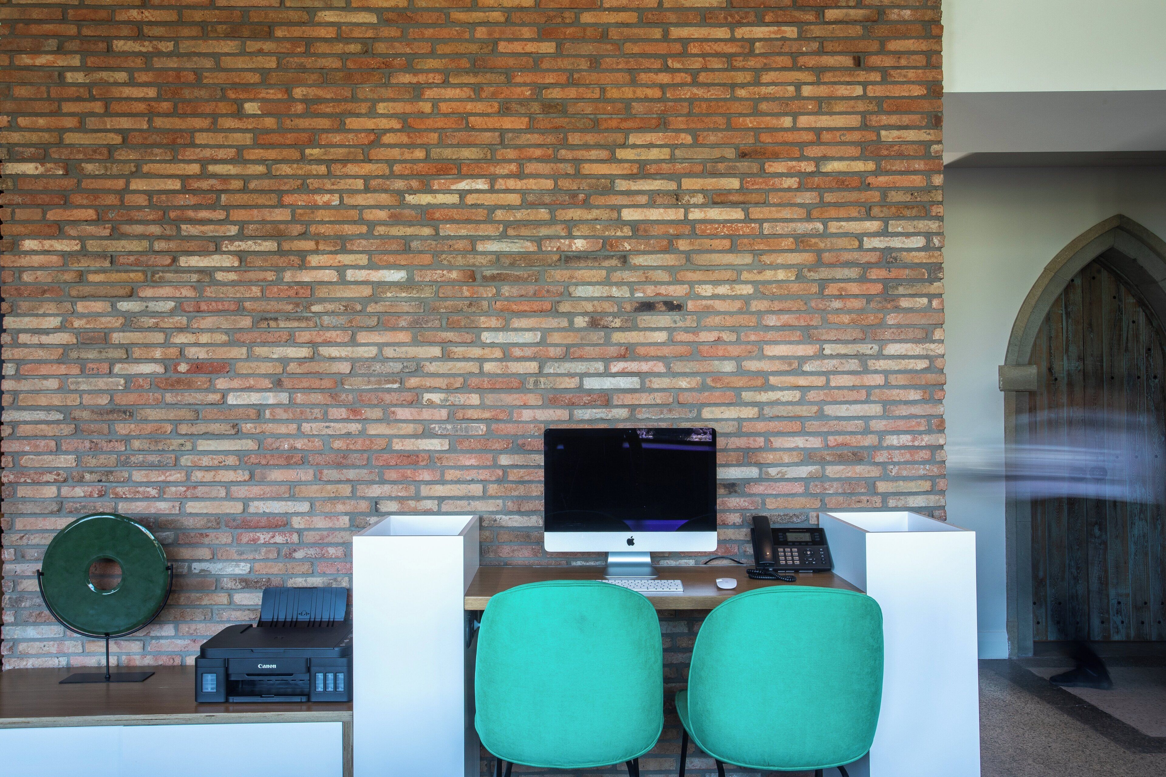 A workspace with a computer, printer, and two chairs against a brick wall.