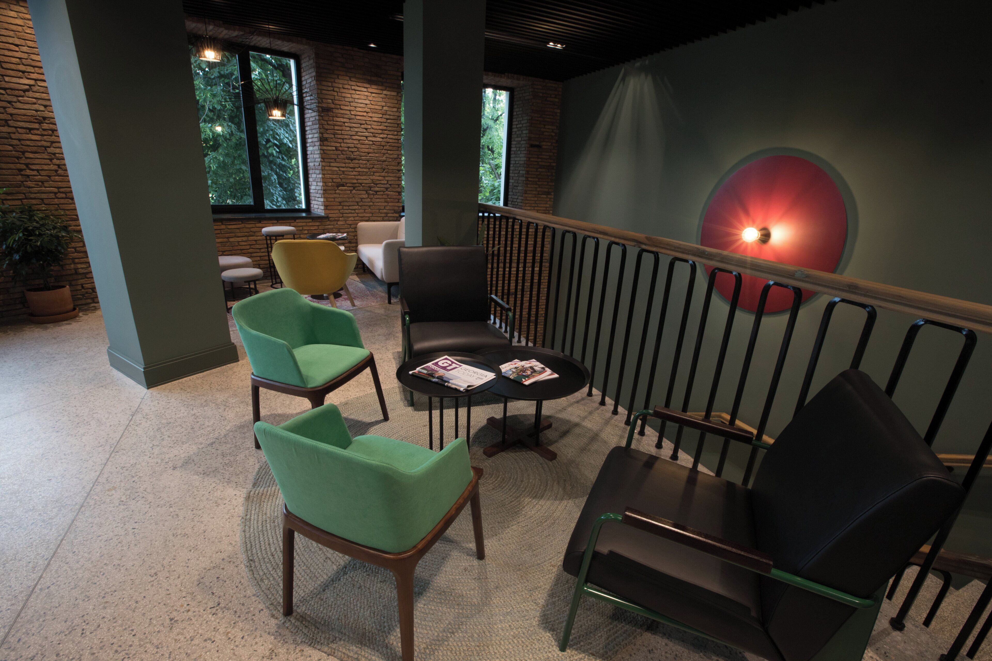 A modern indoor seating area with a mix of chairs and tables, a staircase with a railing, and a large window with a view of greenery.
