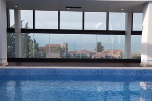 A swimming pool with clear glass walls, offering a view of buildings and trees.
