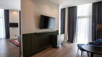 Quarto de hotel moderno com televisão de tela plana na parede, um sofá e uma mesa de jantar.