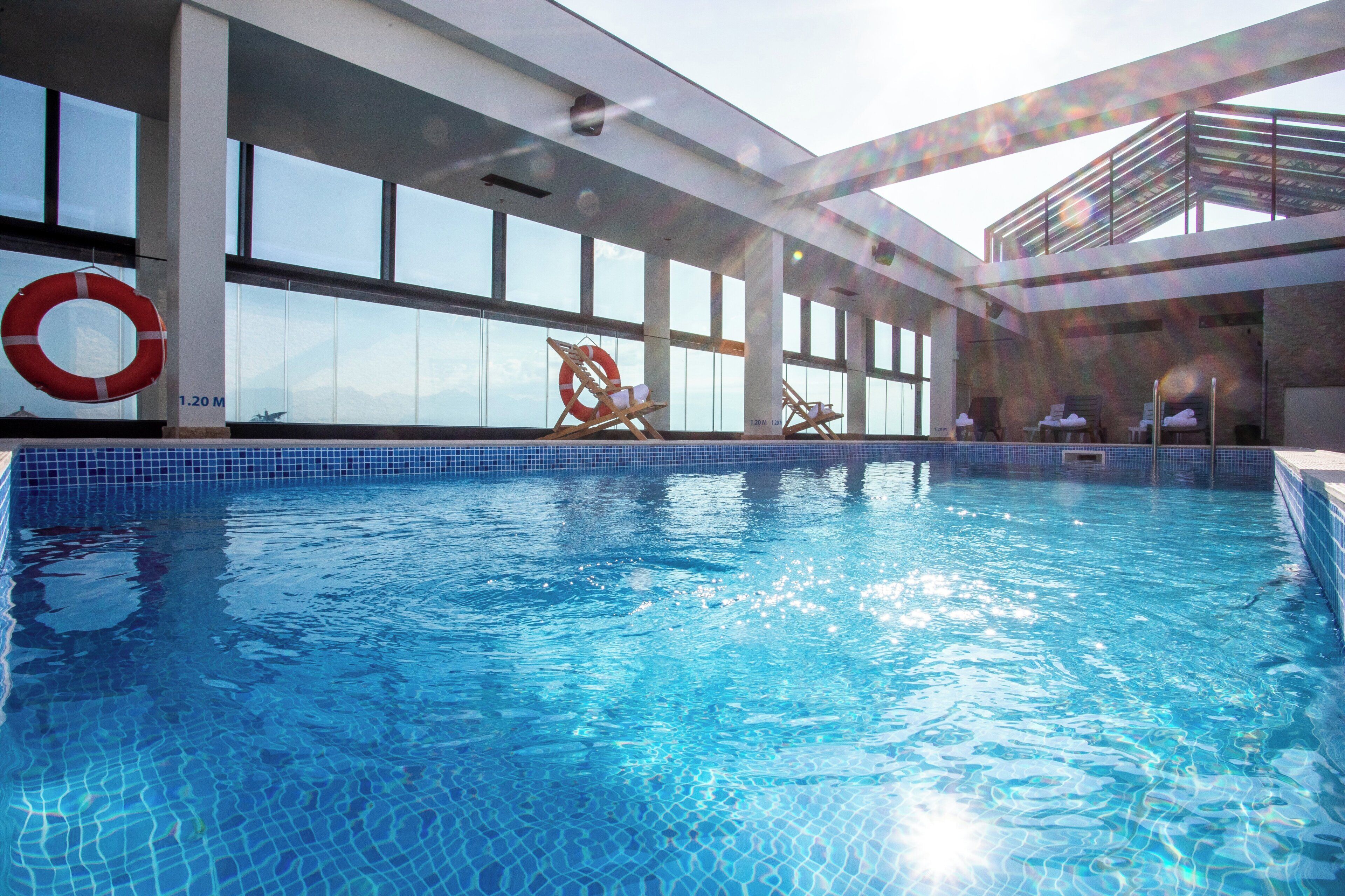 An indoor swimming pool with clear blue water, surrounded by large windows and a lifebuoy.