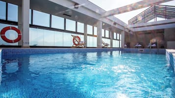An indoor swimming pool with clear blue water, surrounded by large windows and a lifebuoy.