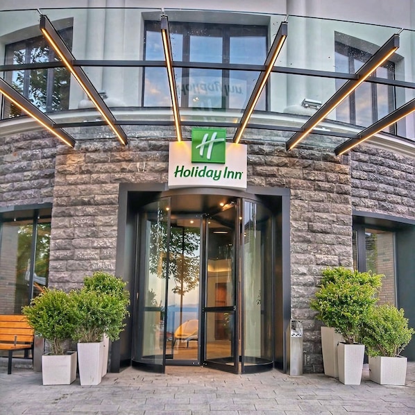 A Holiday Inn entrance with a stone facade, glass doors, and potted plants.