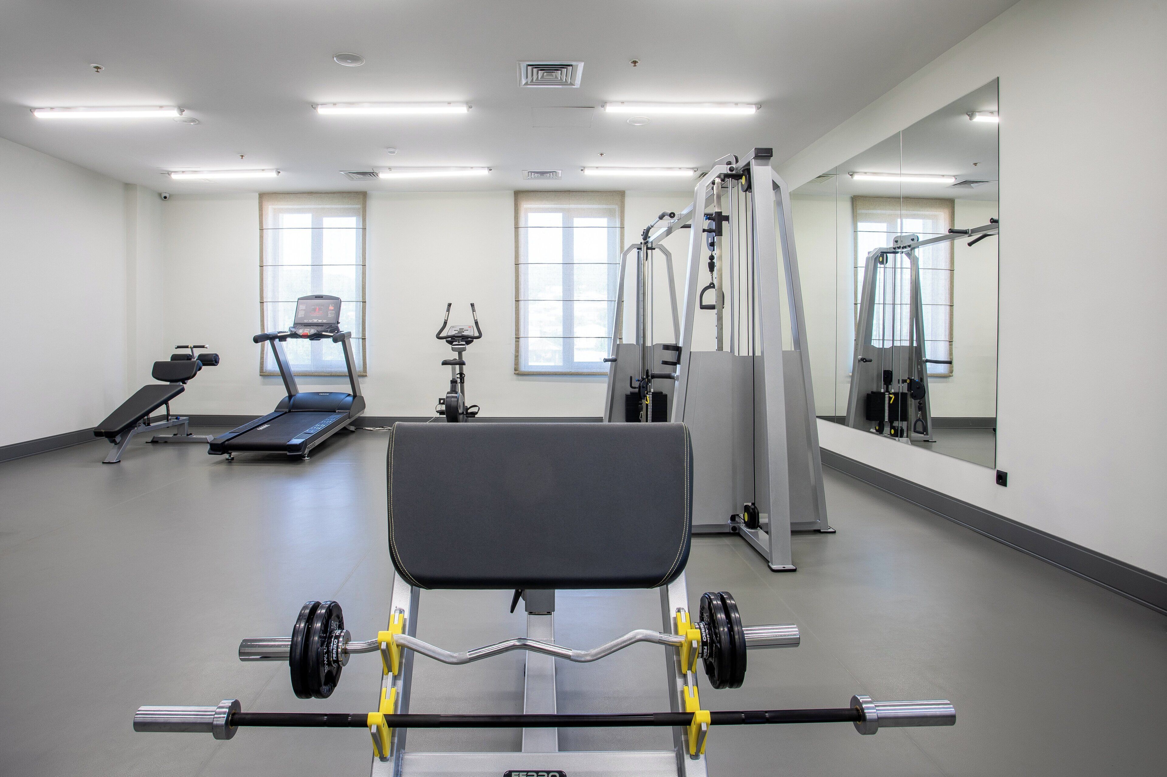 Une salle de sport équipée de matériel d’exercice, notamment un banc de développé couché, des tapis de course et des miroirs.