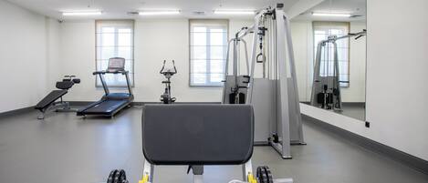 Une salle de sport équipée de matériel d’exercice, notamment un banc de développé couché, des tapis de course et des miroirs.