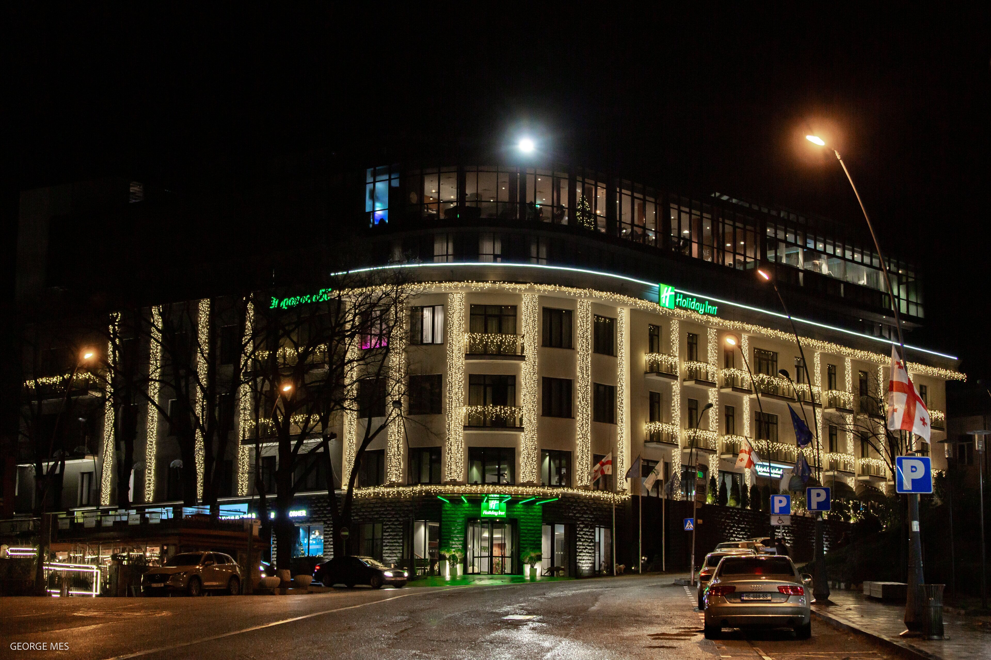 A hotel with a curved facade, illuminated by string lights, and a prominent Holiday Inn sign.