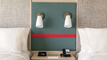 Une chambre d’hôtel avec deux lits, une table de chevet, une horloge numérique, un téléphone et des lampes fixées au mur.