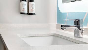 A bathroom with a white sink, a modern faucet, and two hand soap bottles mounted on the wall.