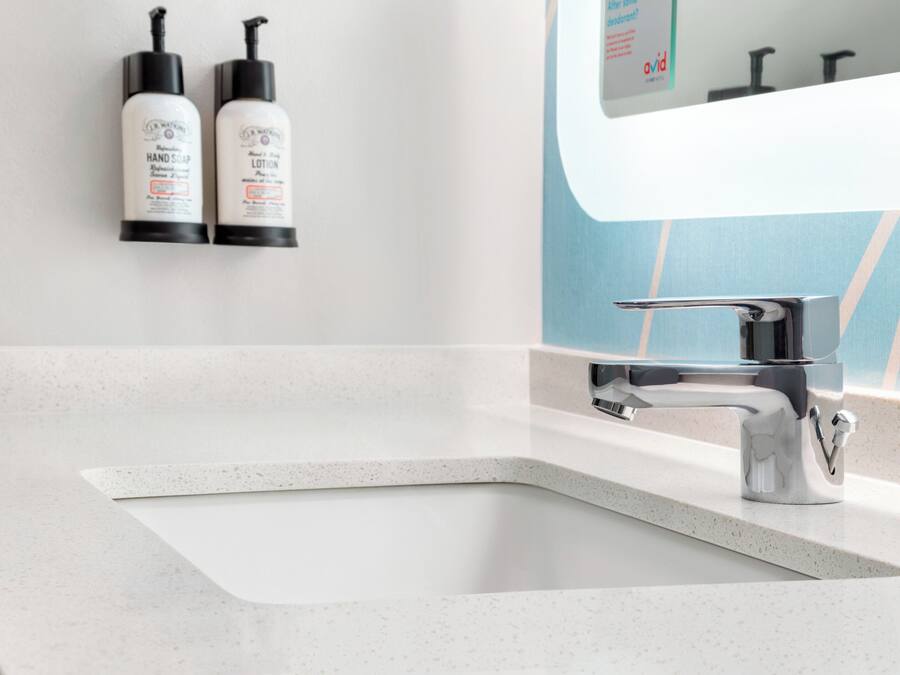 A bathroom with a white sink, a modern faucet, and two hand soap bottles mounted on the wall.