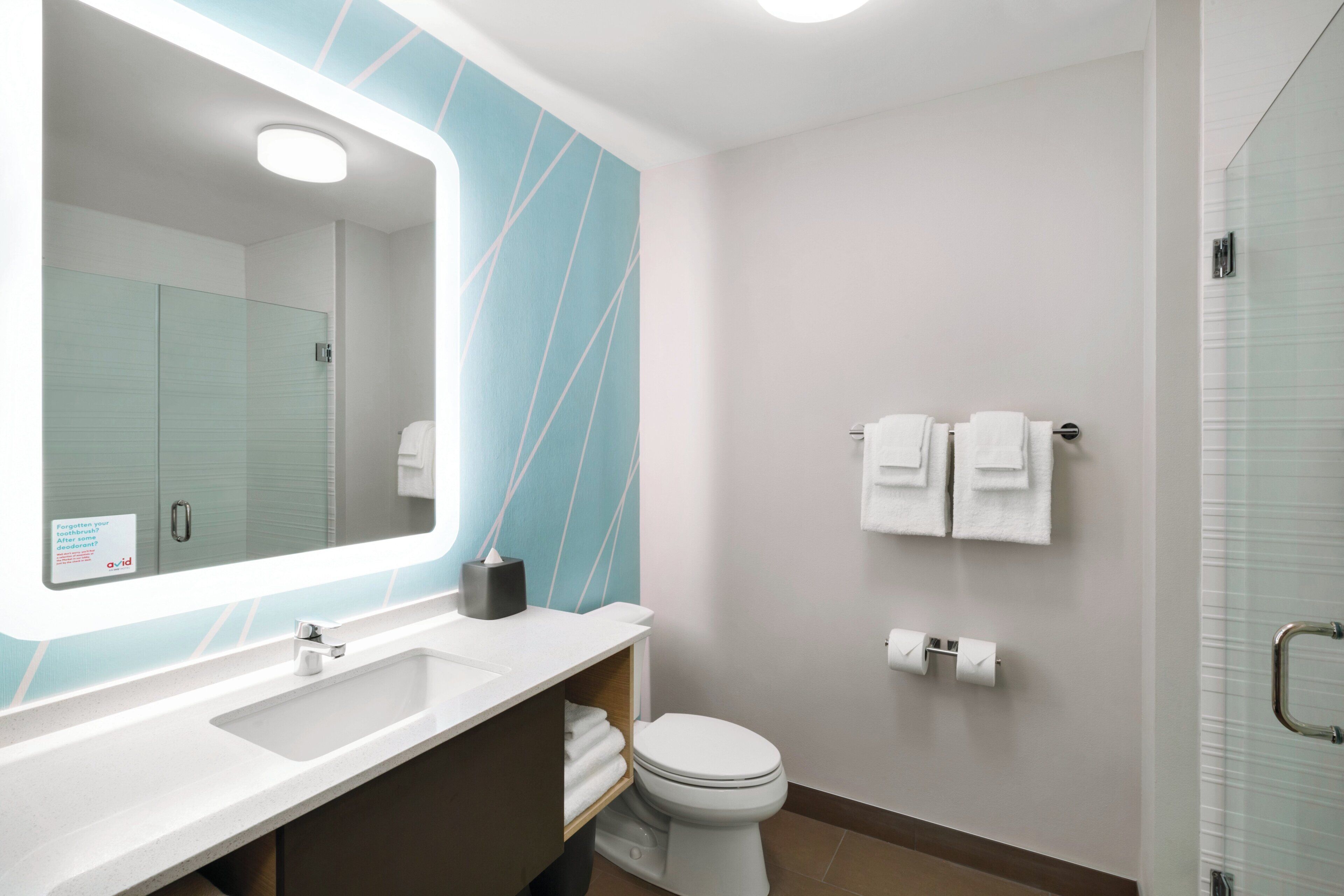 A modern bathroom with a large mirror, a sink, a toilet, and a glass shower enclosure.