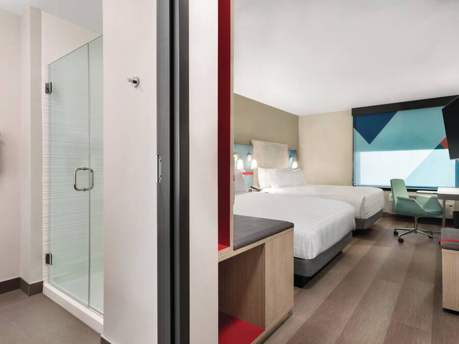 A hotel room with a shower, two beds, a desk, and a TV.