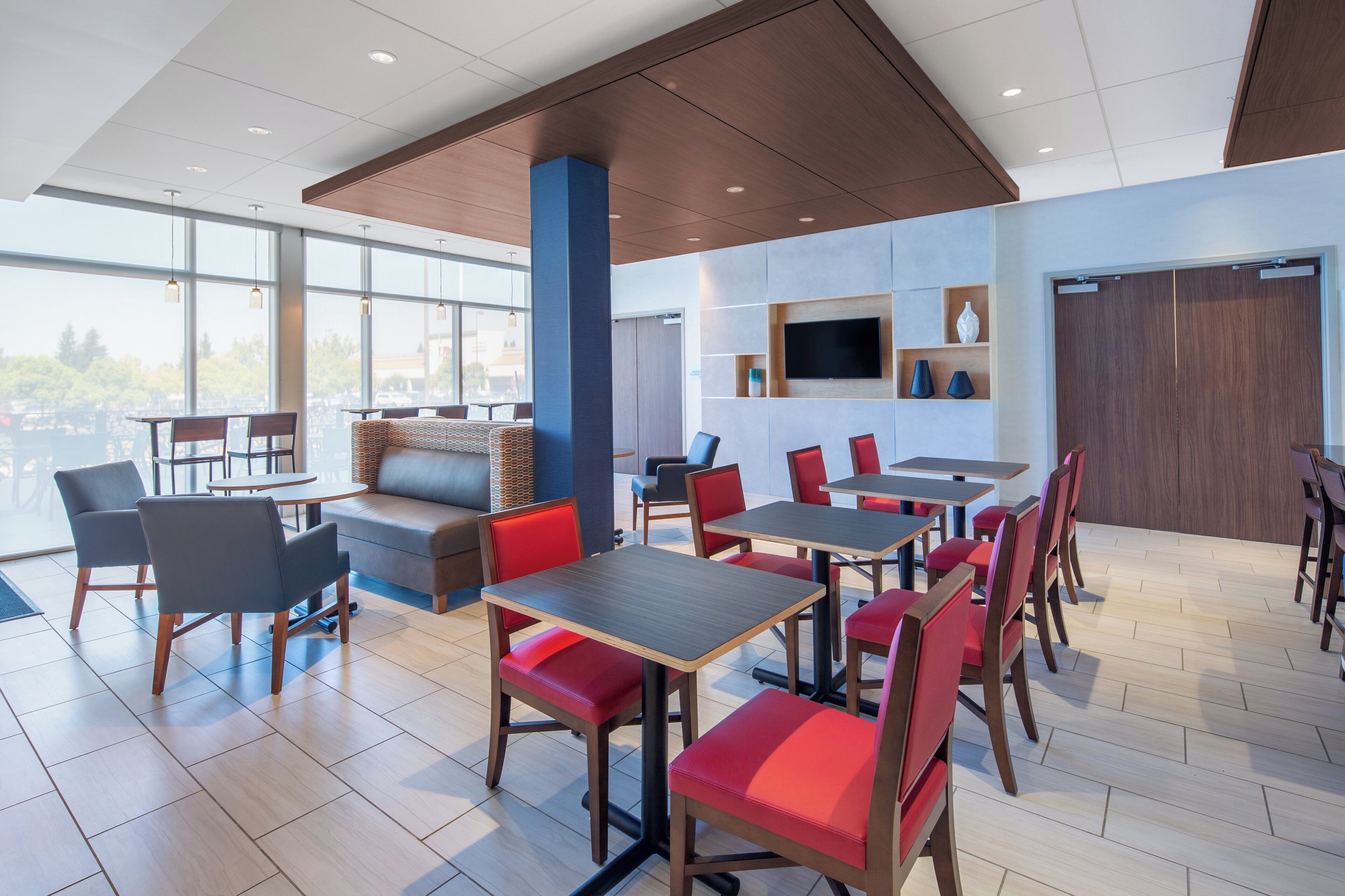 A modern dining area with tables and chairs, a sofa, and a television on the wall.