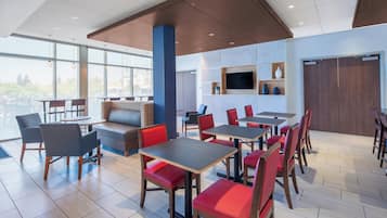 A modern dining area with tables and chairs, a sofa, and a television on the wall.