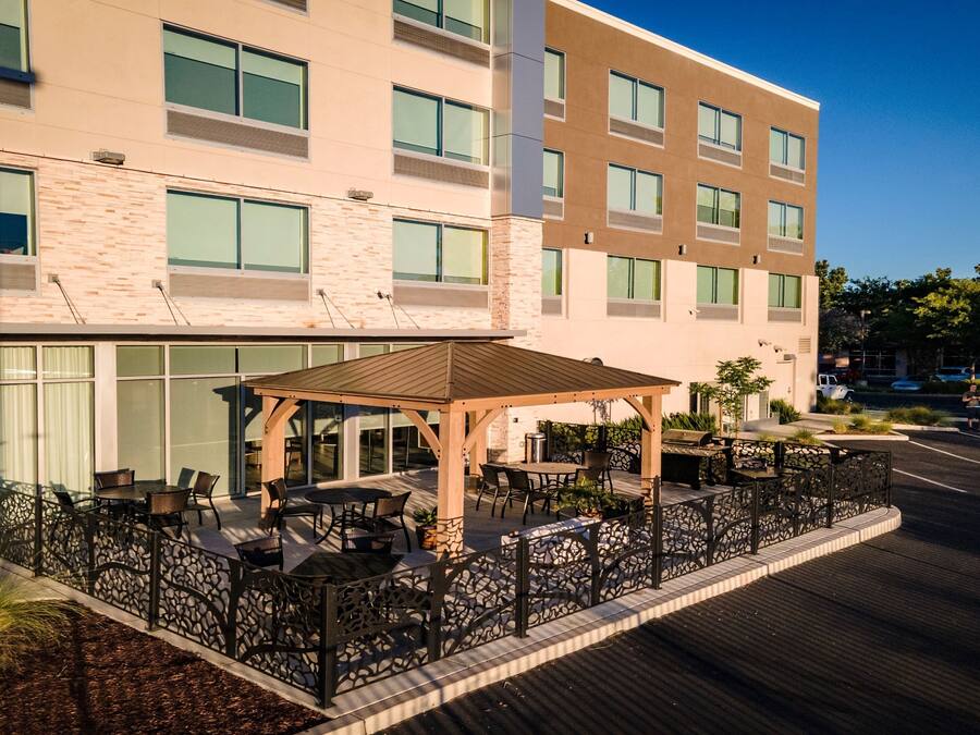 Exterior de un hotel con un patio cubierto, mobiliario al aire libre y una valla de piedra.