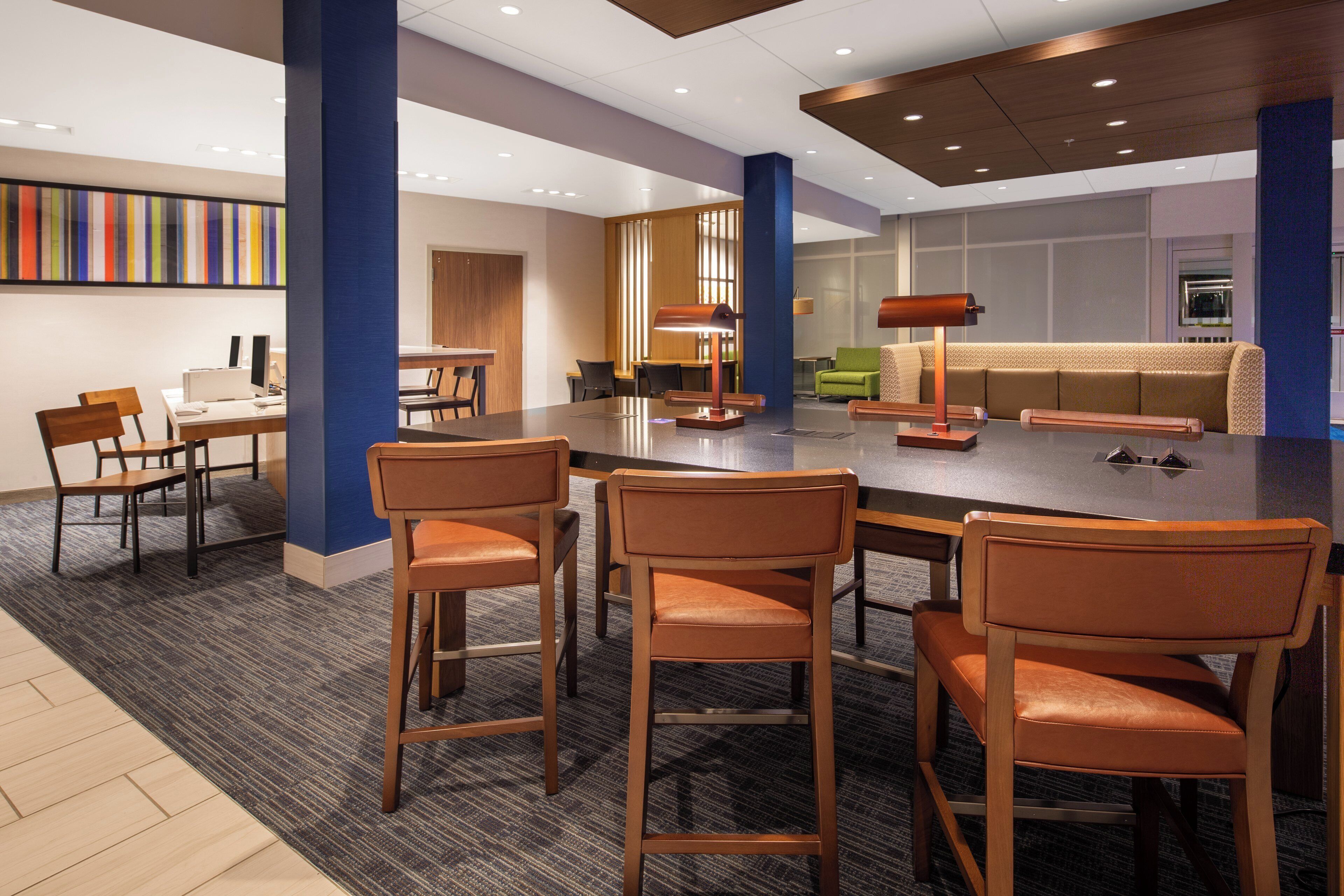 A modern hotel lobby with a central dining area, bar stools, a sofa, and a coffee table.