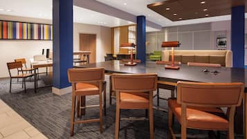 A modern hotel lobby with a central dining area, bar stools, a sofa, and a coffee table.