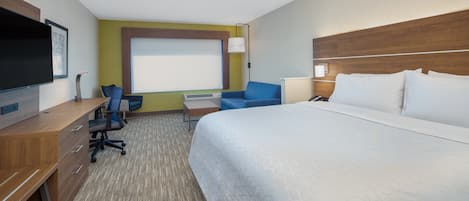 A hotel room with a large bed, a desk with a chair, a TV, and a window with blinds.