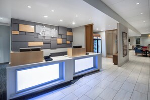 Zona de recepción de hotel con diseño moderno, que incluye un mostrador de recepción, un área de descanso y un refrigerador con bebidas.