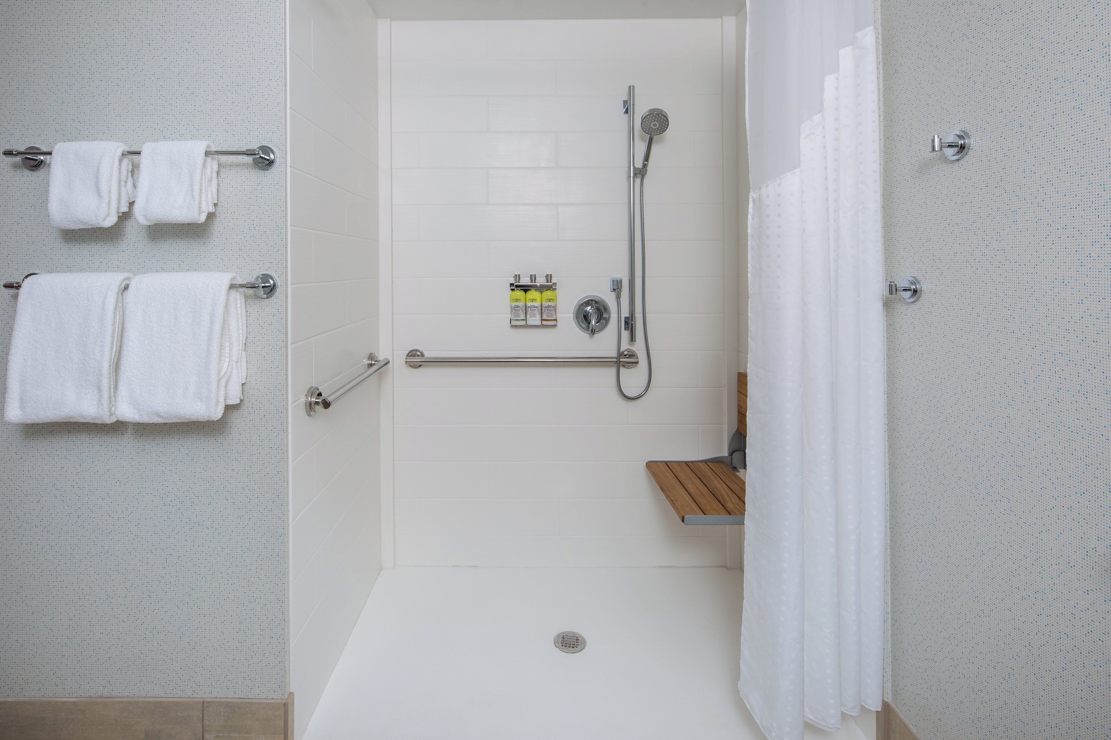 Un baño moderno con ducha a nivel de suelo, inodoro con barra de apoyo y toallero con varias toallas.