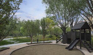 A playground with a slide and climbing structures, surrounded by trees and a paved area. - Holiday Inn Express Beijing Badaling by IHG (Yanqing)