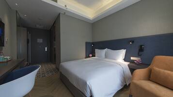A modern hotel room with a large bed, a desk with a chair, and a small sofa.