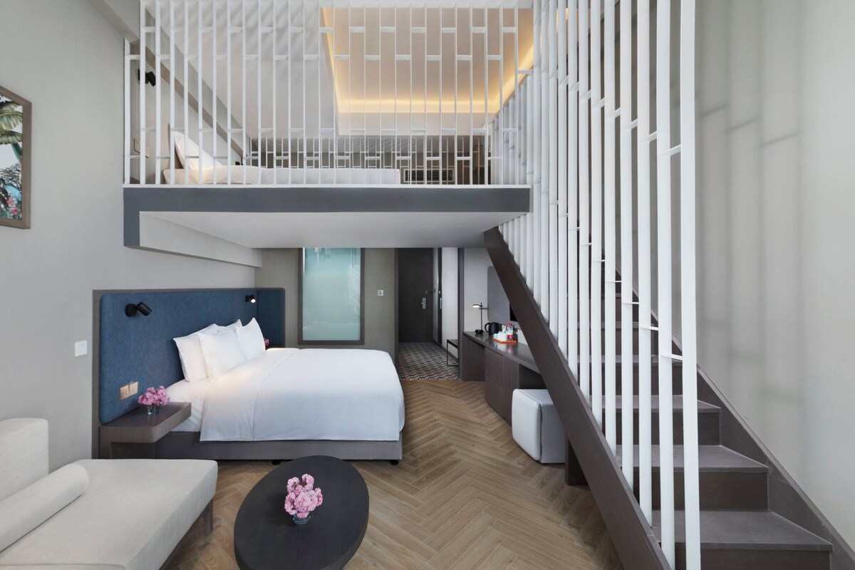 A modern hotel room with a bed, a sofa, a coffee table, and a staircase.