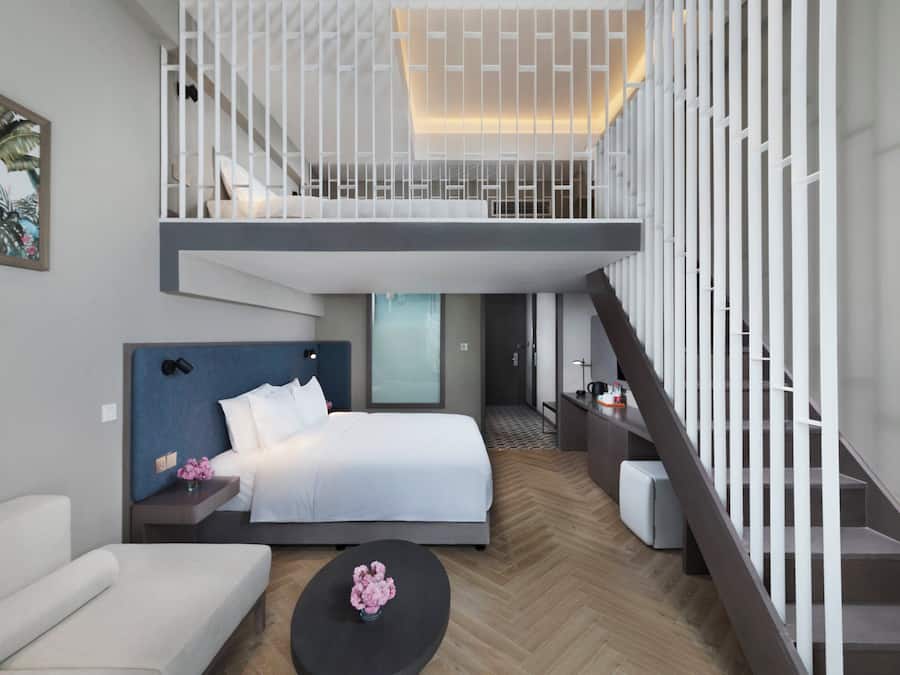 A modern hotel room with a bed, a sofa, a coffee table, and a staircase.