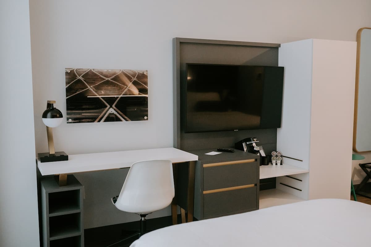 A modern hotel room with a flat-screen TV, a desk with a chair, a bed, and a wall-mounted artwork.