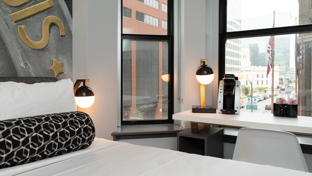 A hotel room with a bed, a desk with a coffee maker, and a window with a city view.