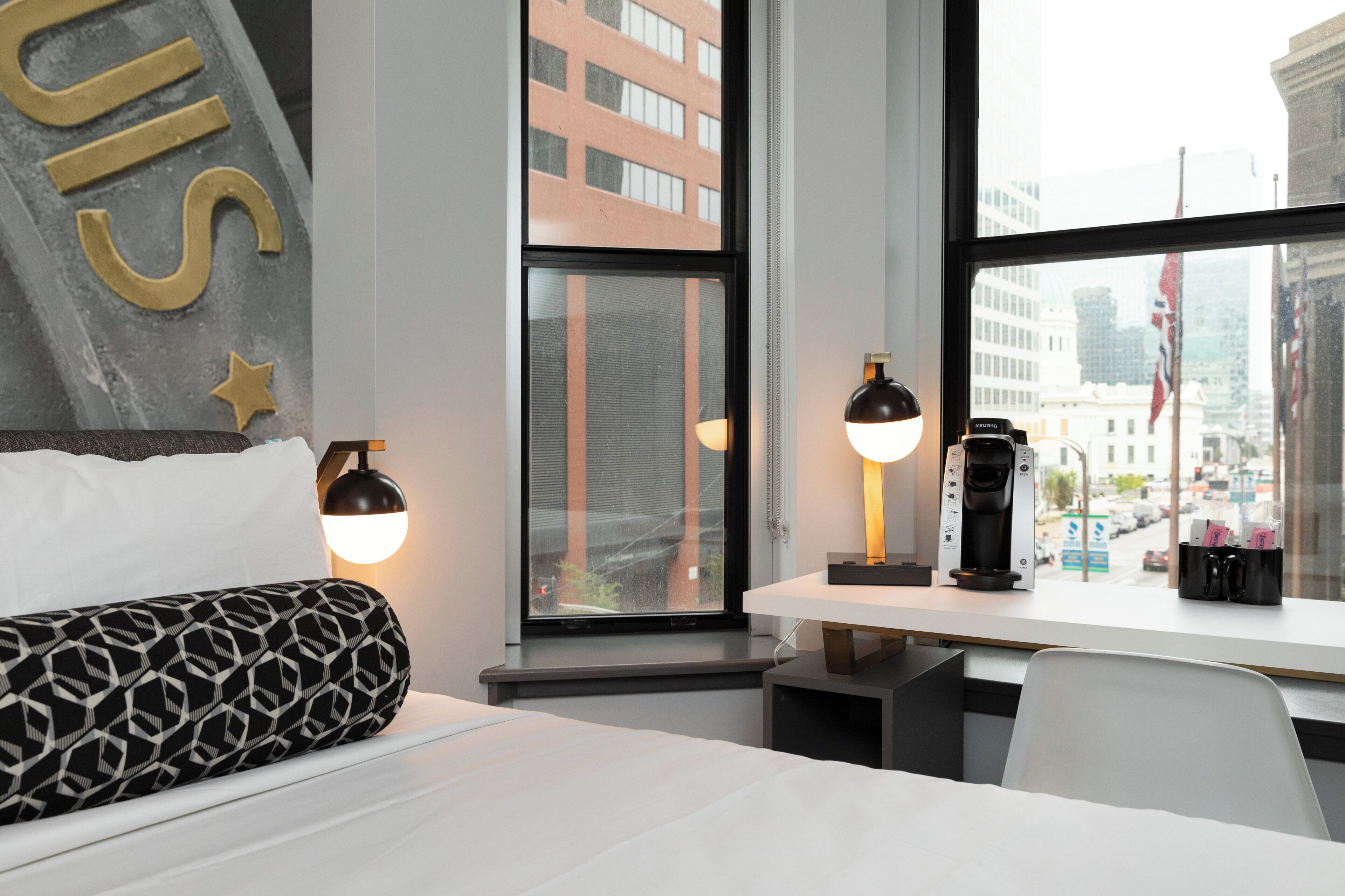 A hotel room with a bed, a desk with a coffee machine, and a window with a city view.