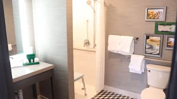 Un baño moderno con ducha, inodoro y lavamanos. Hay toallas colgadas en la pared y un cuadro enmarcado.