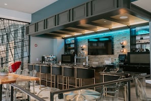A modern bar area with a brick wall, bar stools, and a large TV screen. - Hotel Indigo St. Louis - Downtown by IHG (St. Louis)